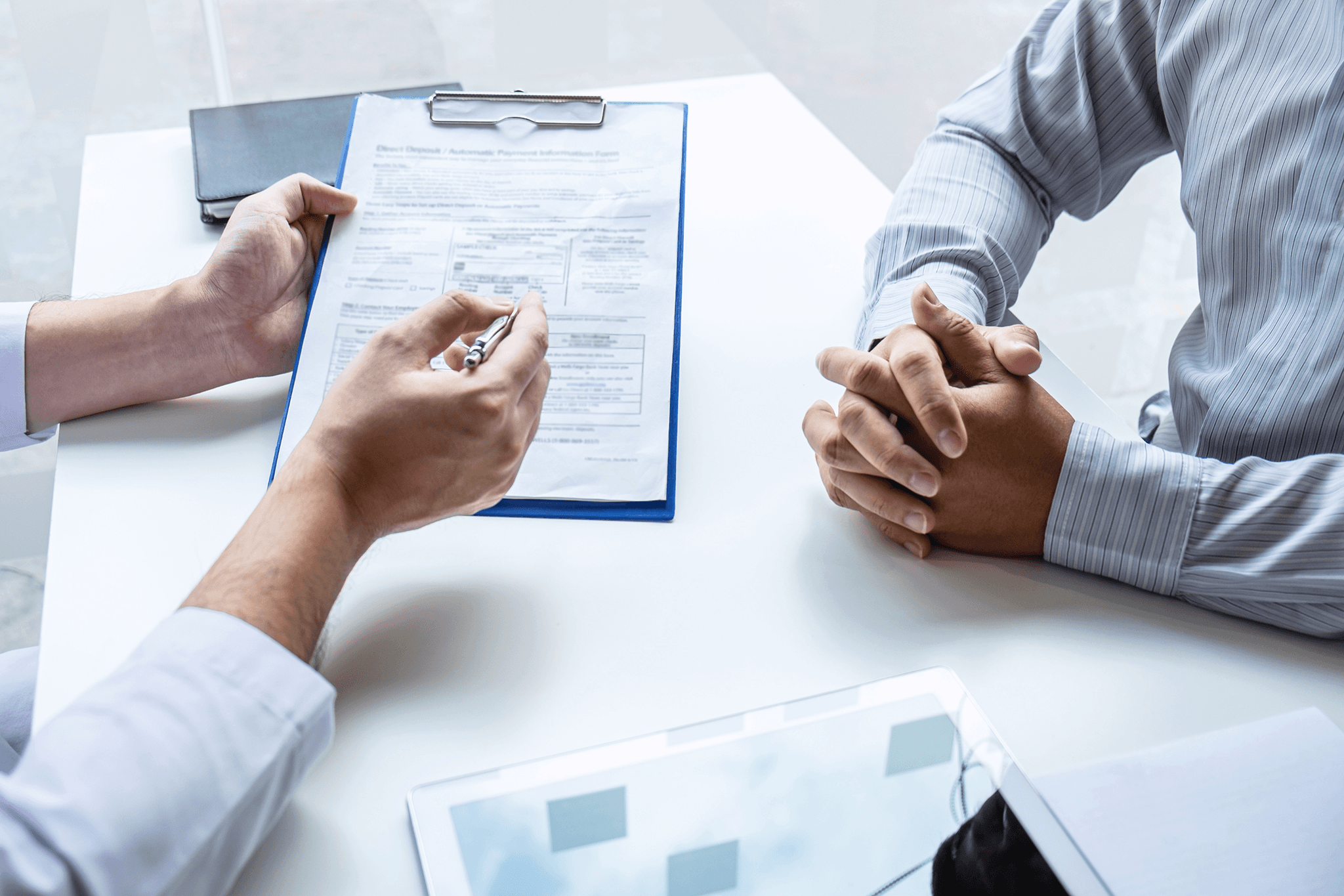 Two people reviewing a document across a desk during a consultation, one holding a clipboard and pen